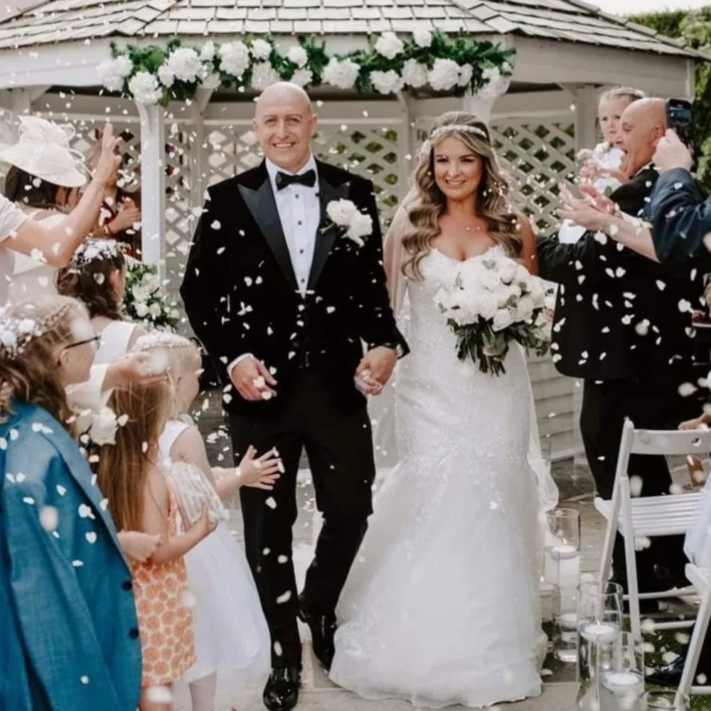 Groom in a bespoke black tuxedo and bow tie with his bride at an outdoor ceremony