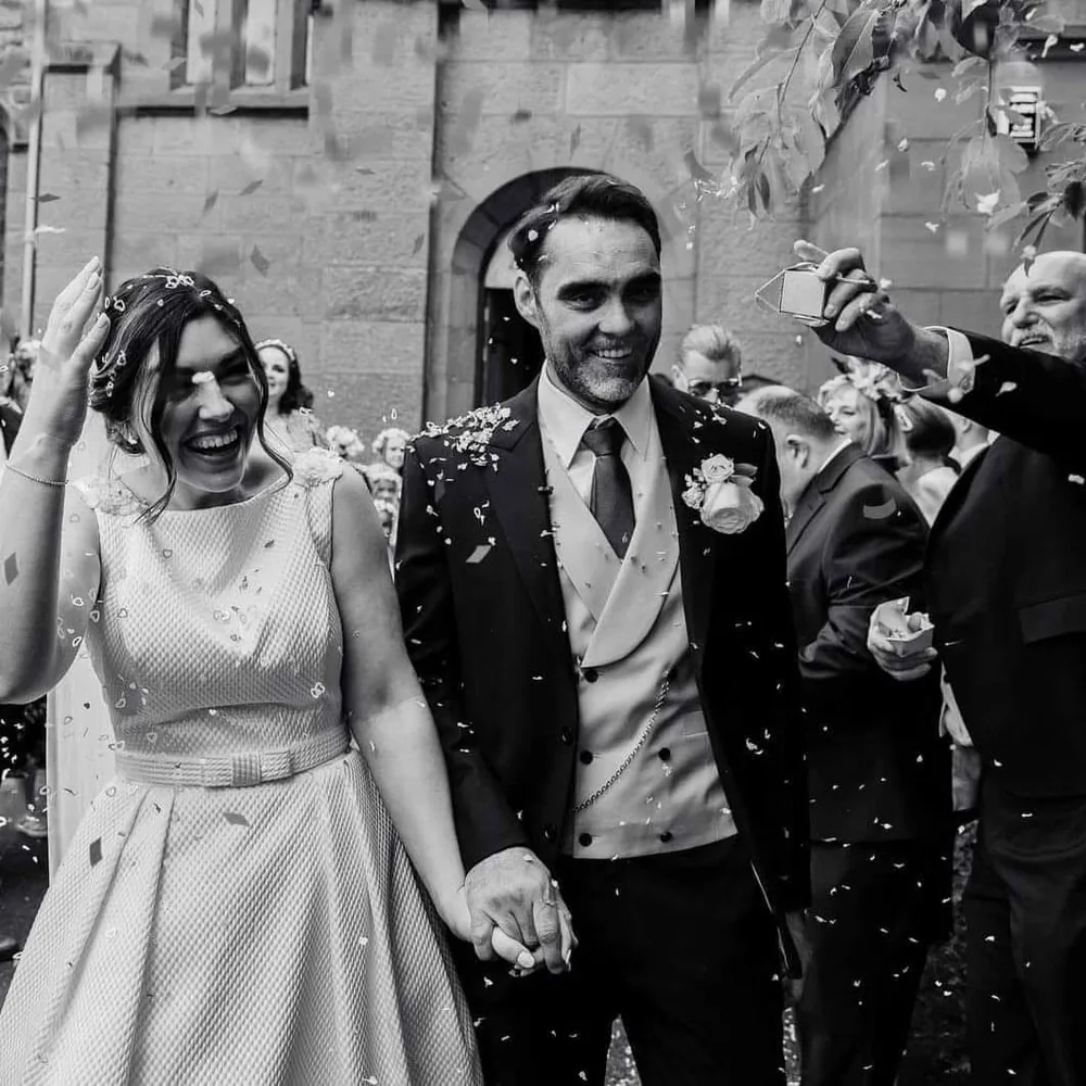Groom in a bespoke three-piece suit with his bride during the confetti walk